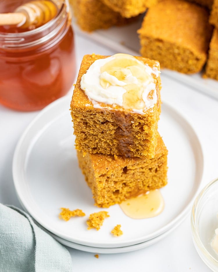 A stack of two pieces of pumpkin corn bread with butter and honey on top