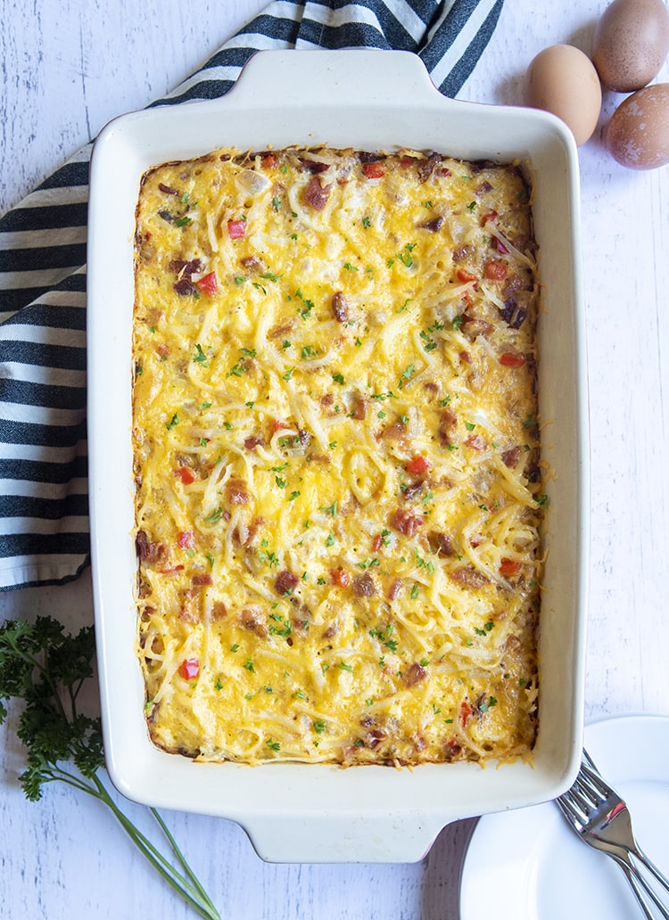 A whole pan of breakfast casserole photographed from above, showing the cheese, some bacon bits, and red pepper on top, and sprinkled with parsley.