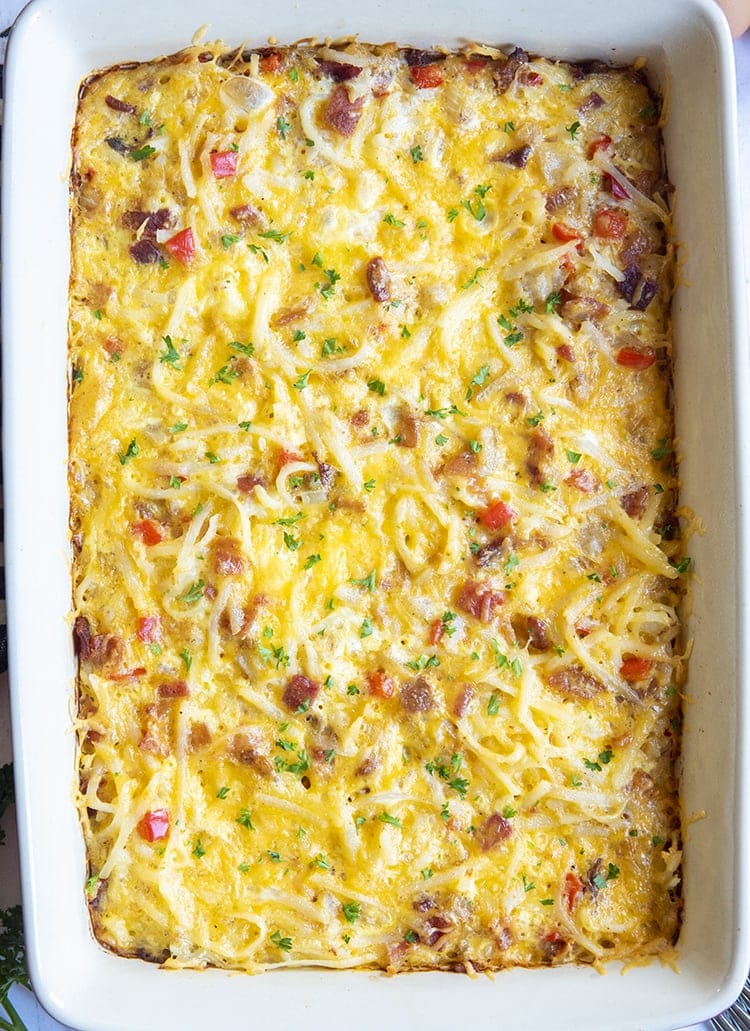 A whole pan of breakfast casserole photographed from above, showing the cheese, some bacon bits, and red pepper on top, and sprinkled with parsley.