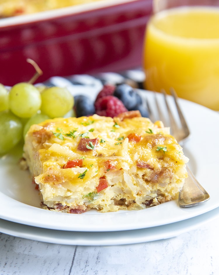 A close up of a breakfast casserole on a plate with berries and grapes in the background.