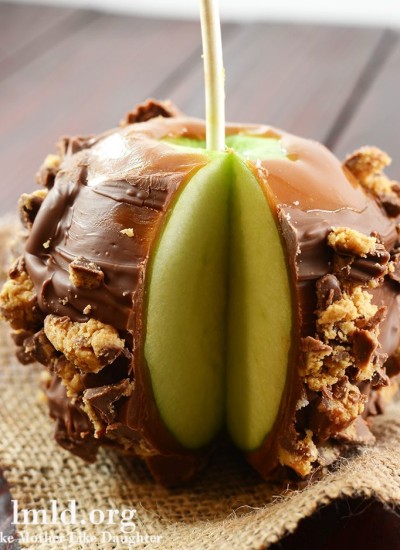 Front view of a candy coated caramel apple with a slice removed.
