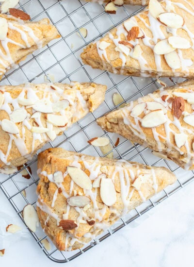 A wire rack topped with almond apple scones, with a glaze, and sliced almonds on top.