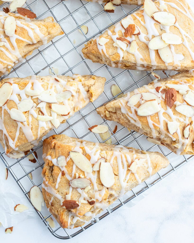 A wire rack topped with almond apple scones, with a glaze, and sliced almonds on top.