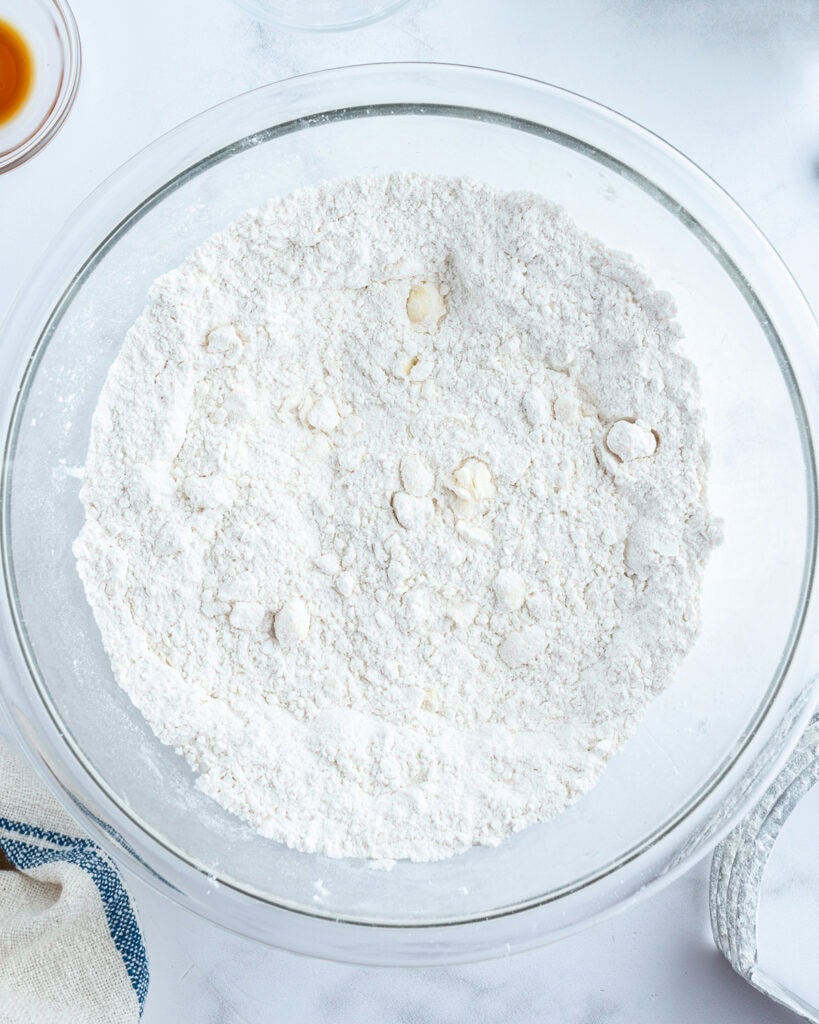 A bowl of flour mixture with small bits of butter throughout.