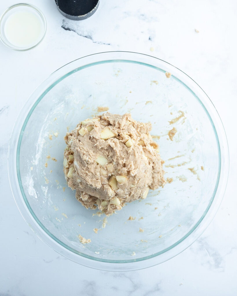 A bowl of a wet dough full of apple pieces.