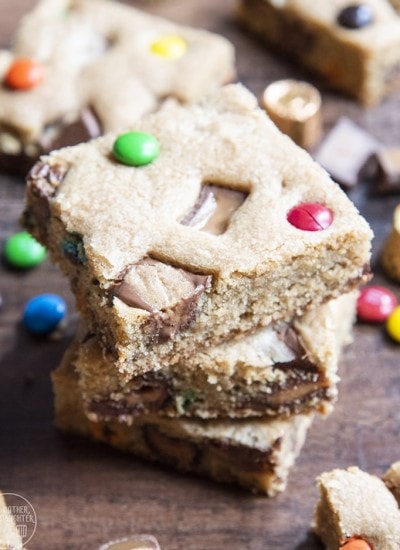 A stack of three cookie bars full of candy bar pieces and m&ms.