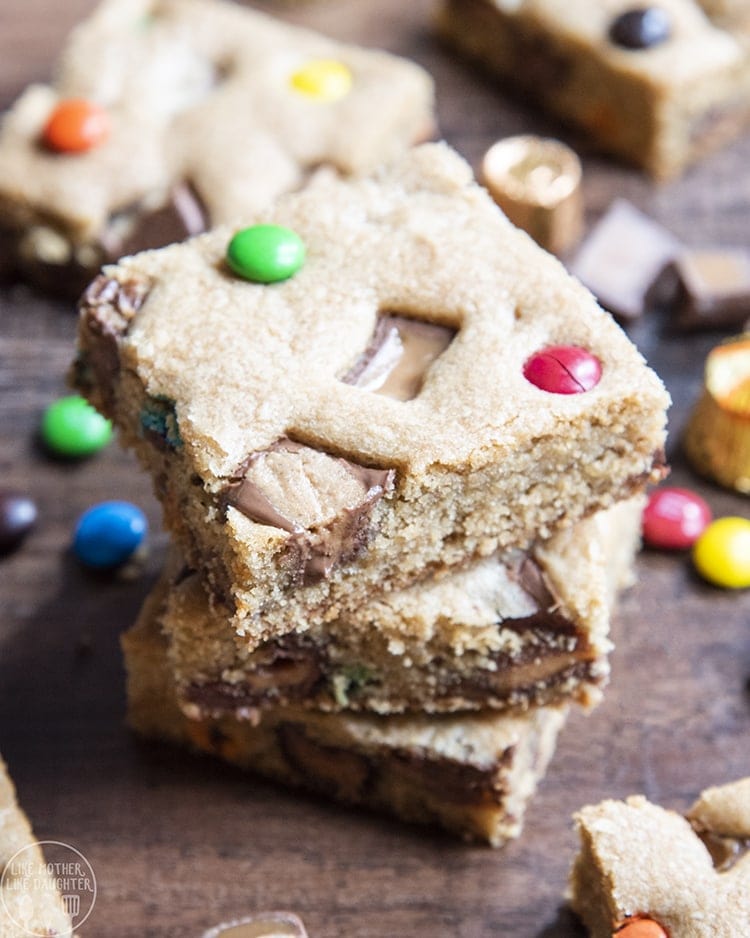 A stack of three cookie bars full of candy bar pieces and m&ms.