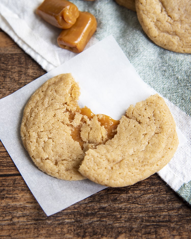 A cookie on a piece of parchment paper being torn apart and showing caramel in the middle.