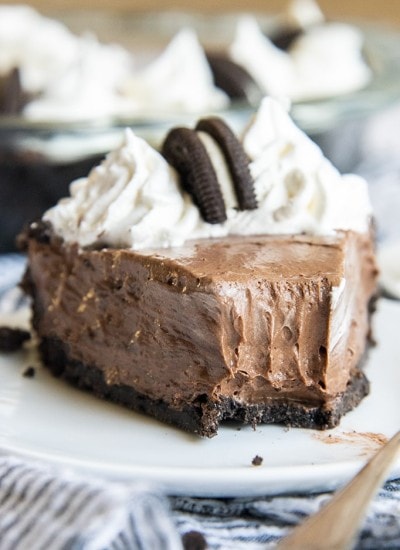 A piece of chocolate cream pie on a white plate with a bite taken out of it.