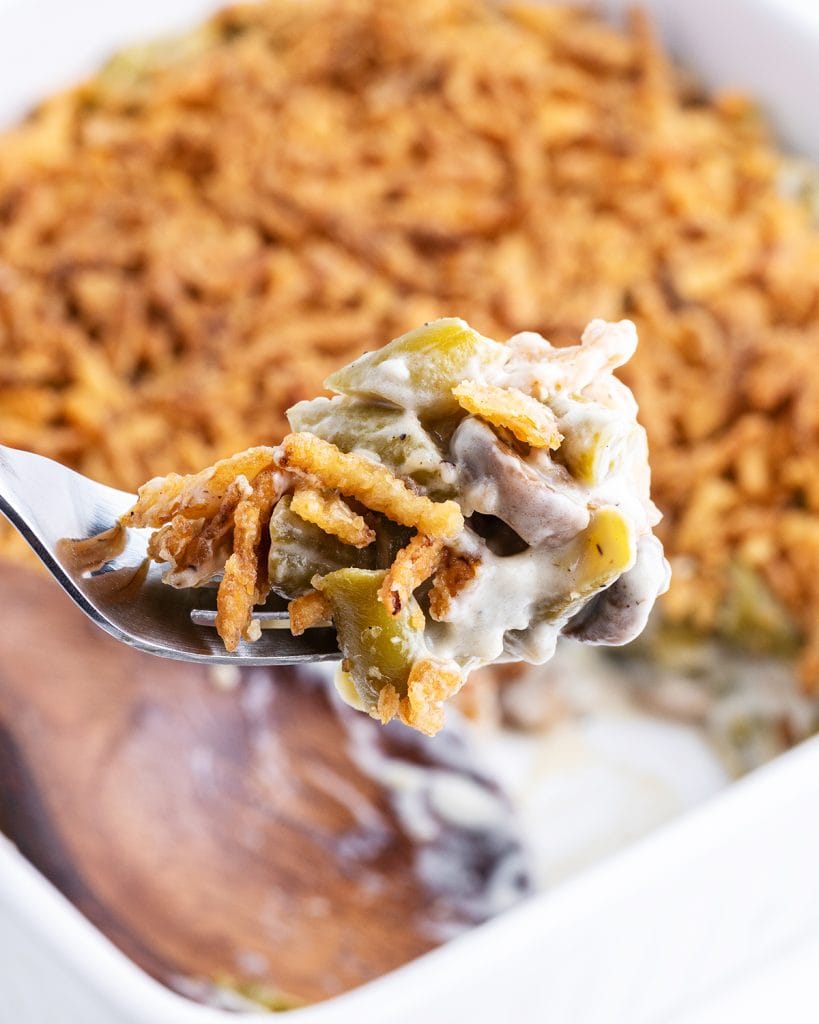 A spoonful of green bean casserole with green beans, creamy mushroom gravy, and crispy fried onions on top.