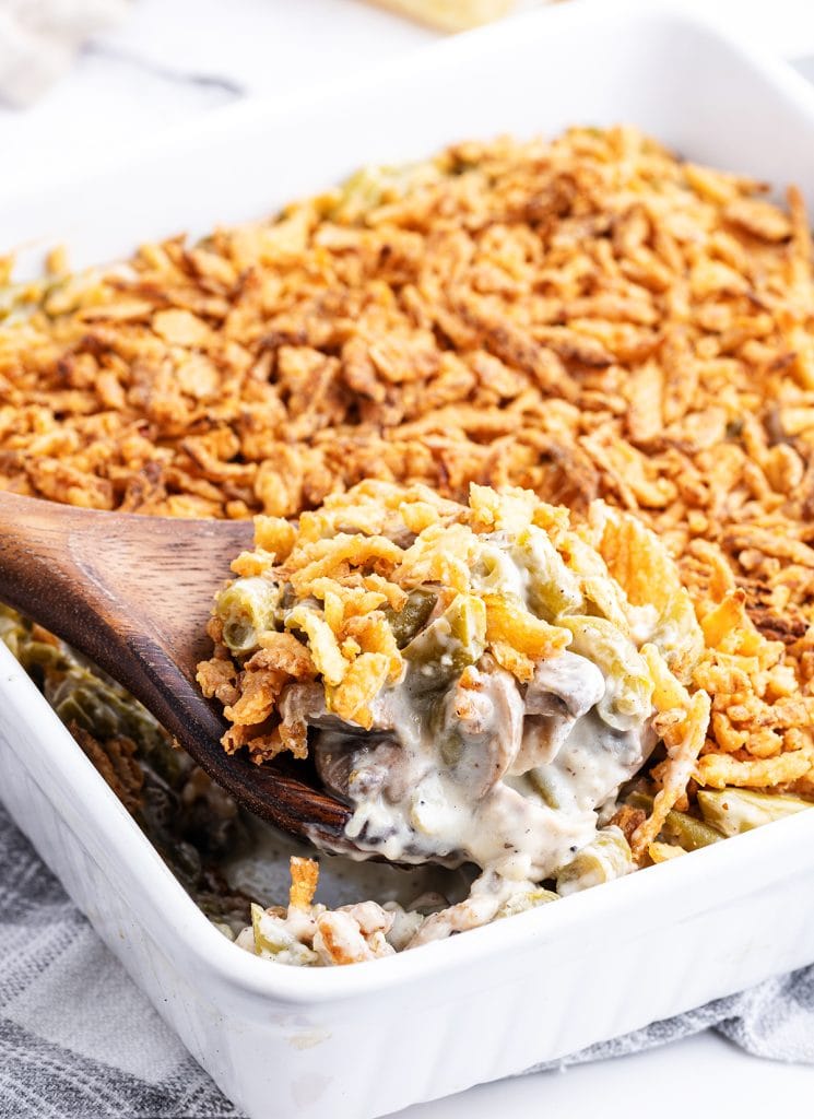 A wooden spoon lifting green bean casserole out of a baking pan.
