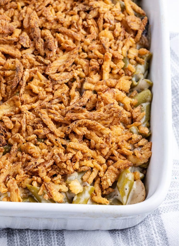 A white baking dish full of green bean casserole with crispy fried onions on top.