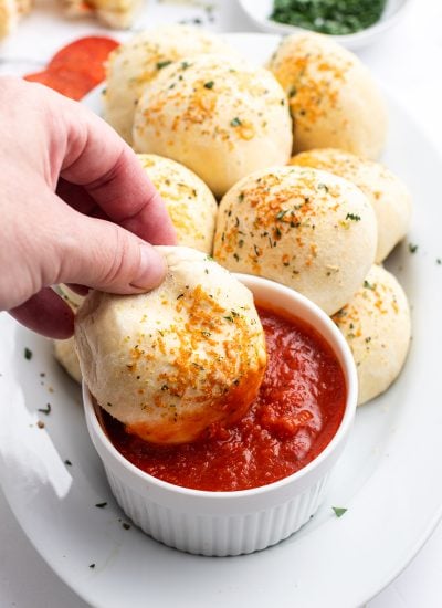 A hand dipping a pizza roll into a bowl of marinara sauce.