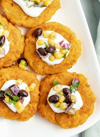 Round sweet potato patties on a white plate topped with sour cream, and a corn salsa.