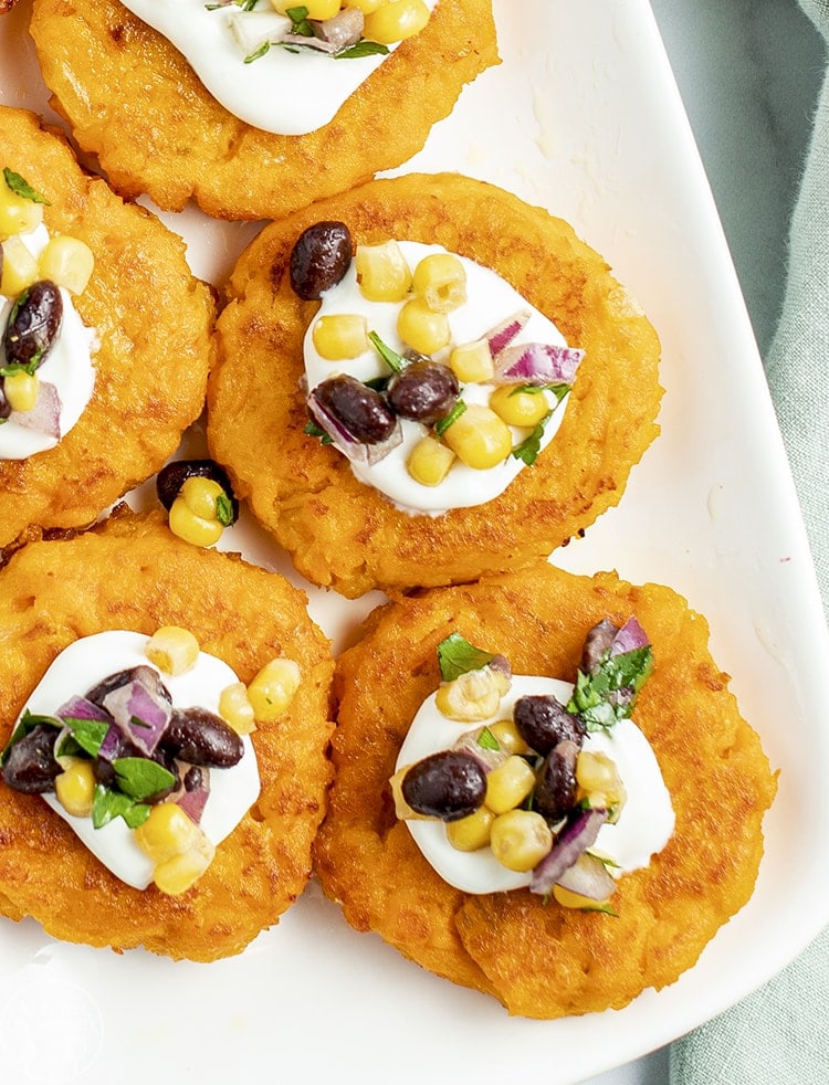Round sweet potato patties on a white plate topped with sour cream, and a corn salsa.