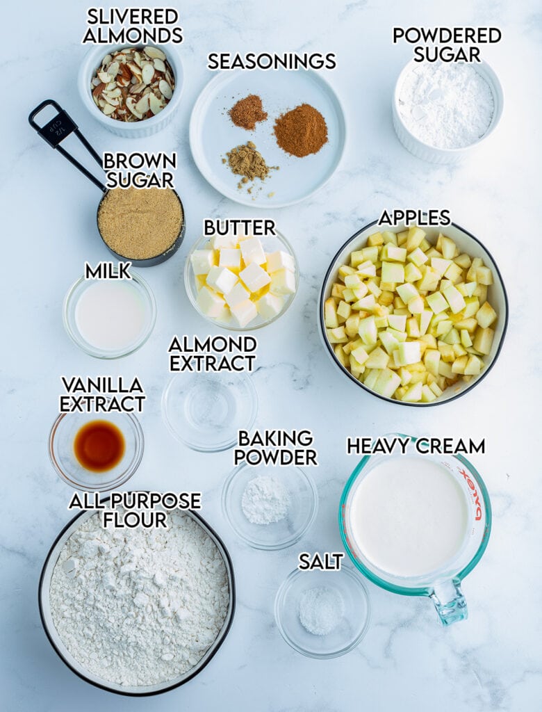 Small bowls full of the ingredients needed to make apple scones, with apples, flour, almond extract, butter, and seasonings.