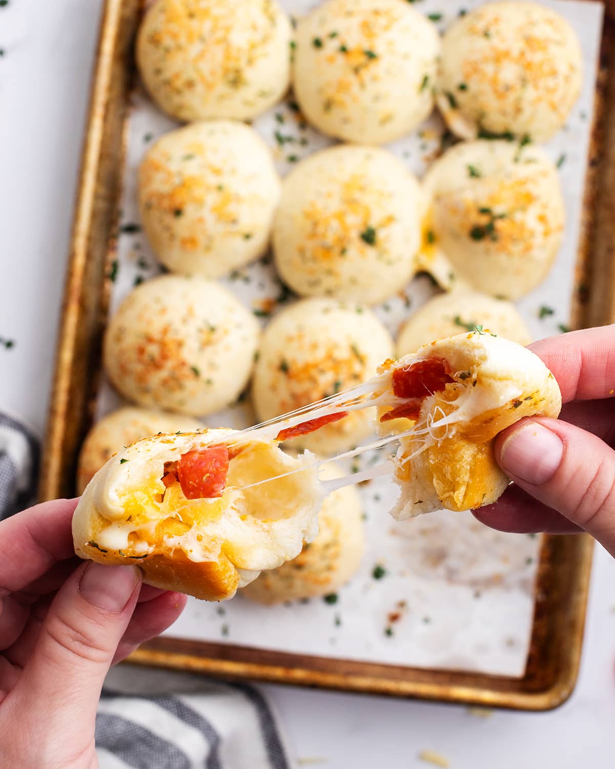 A hand holding two halves of a stuffed pizza roll showing the cheese and pepperoni in the middle.