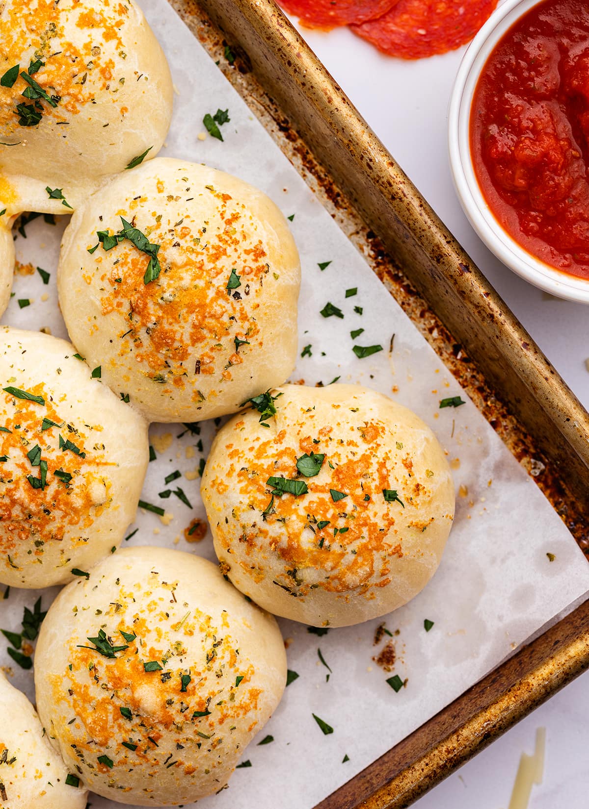 A close up of baked stuffed pizza rolls on a baking pan next to a bowl of marinara sauce.