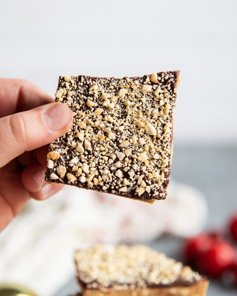 A kid's hand holding a piece of toffee coated in chocolate and cashews.