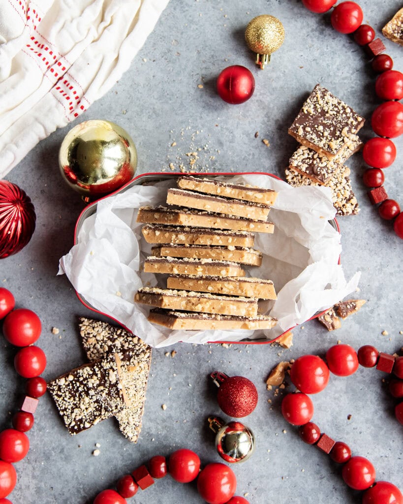 Homemade toffee with cashews stacked in a row in a metal tin.