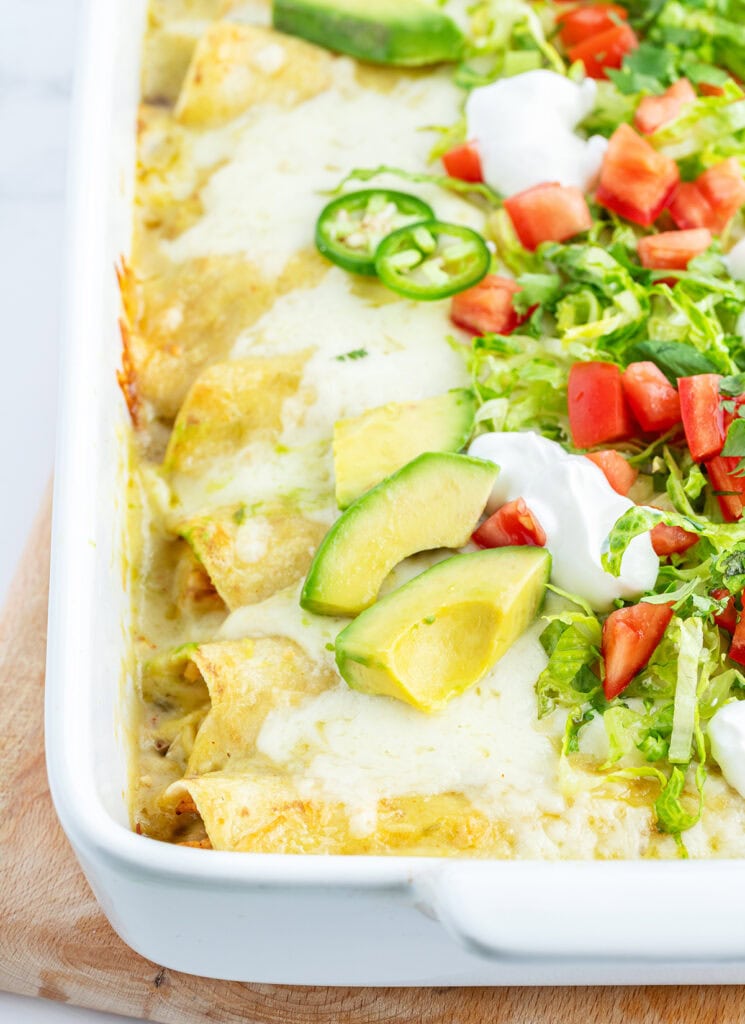 A pan of honey lime chicken enchiladas topped with lettuce, avocado, and tomatoes.