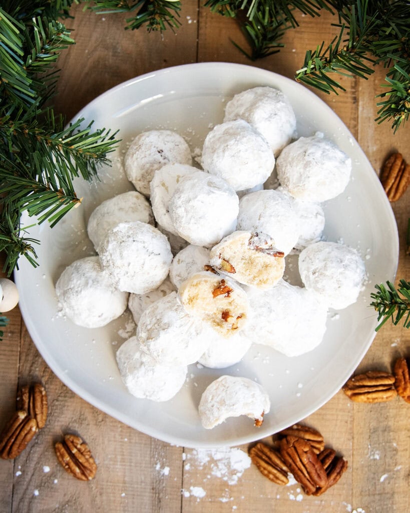 A plate of snowball cookies, and one cookie is cut open showing both halves of the middle. 