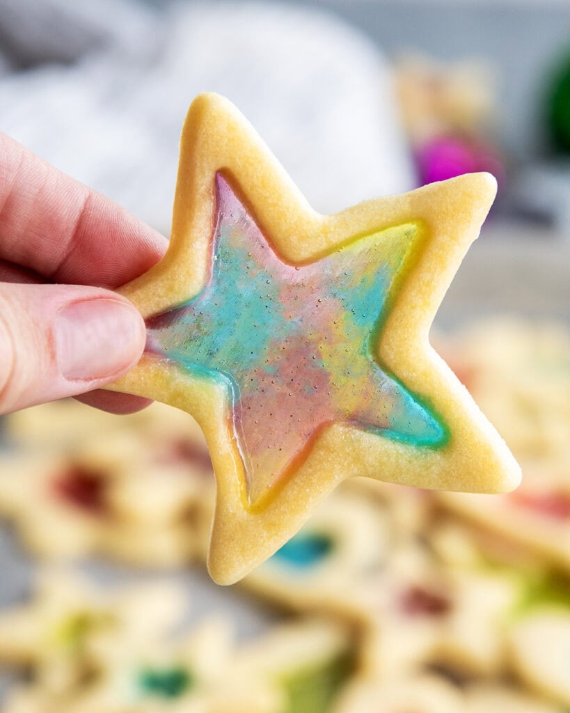 A hand holding a tie dye stained glass window star cookie.