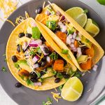 Two corn tortillas filled with sweet potatoes, black beans, red onion, avocado and cilantro.