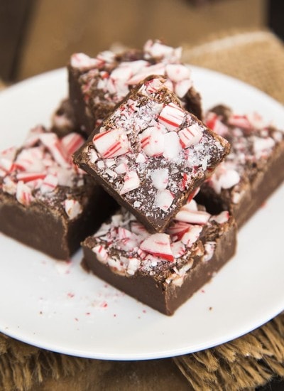 A plate with a pile of peppermint fudge pieces. It is chocolate mint fudge topped with candy cane pieces.