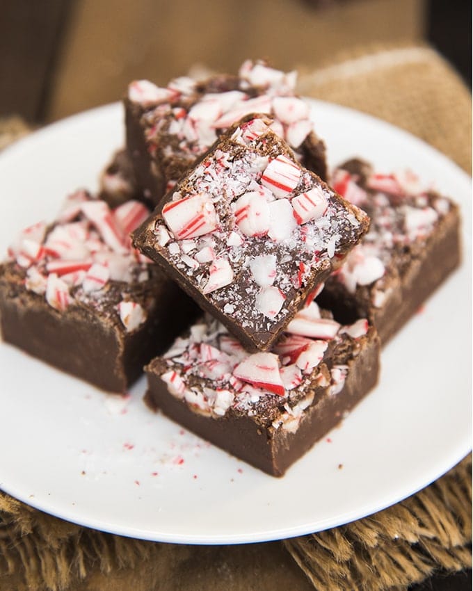 A plate with a pile of peppermint fudge pieces. It is chocolate mint fudge topped with candy cane pieces.