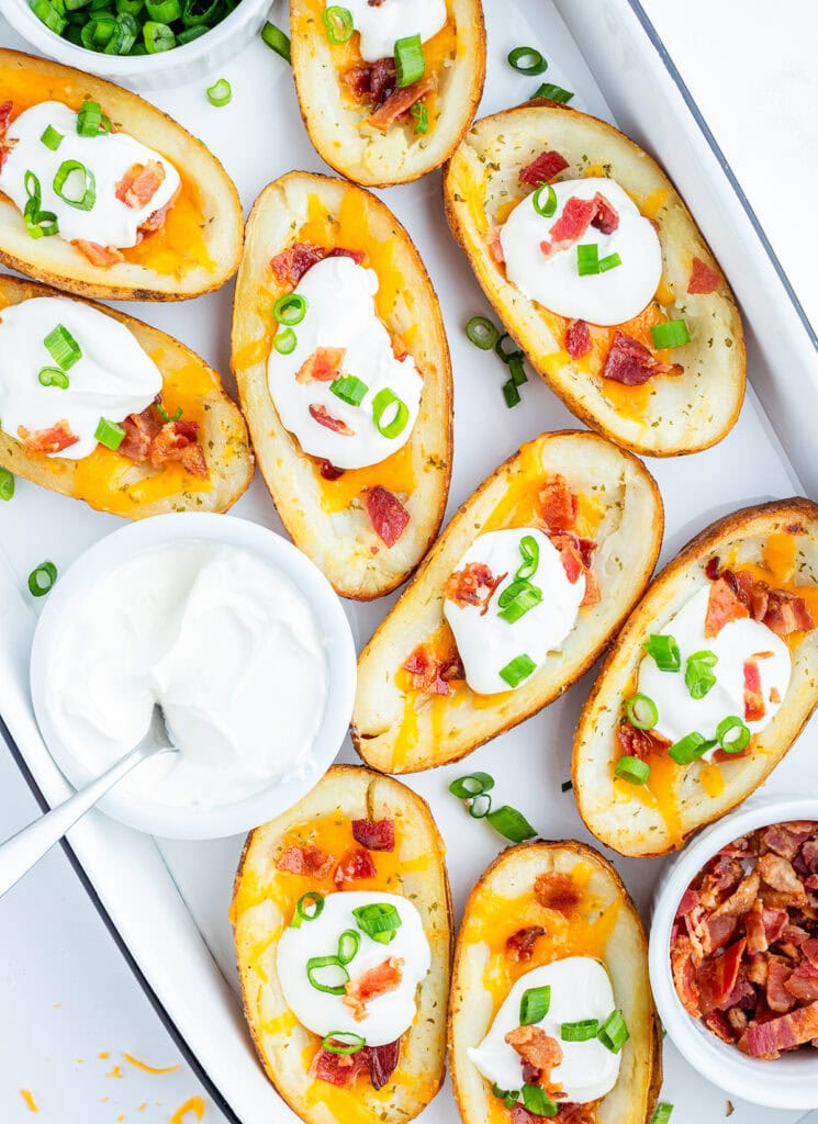 A tray of baked potato skins topped with cheese, sour cream, and bacon.