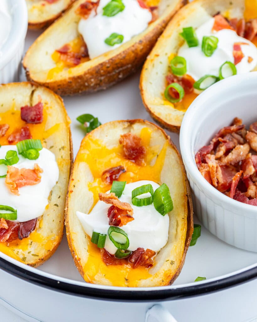 A close up of baked potato skins topped with cheese, sour cream, bacon, and green onions.