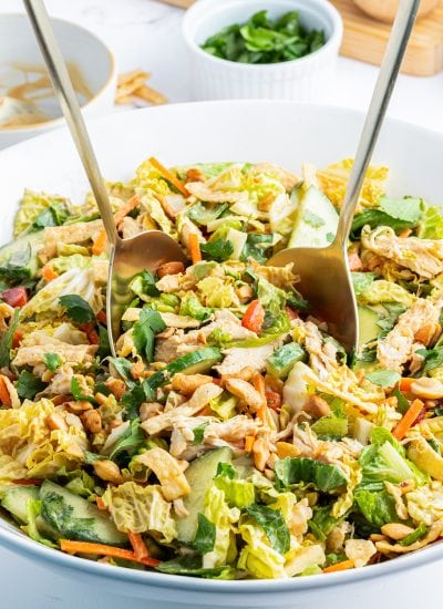 A bowl of Thai chicken salad with two mixing spoons in it.