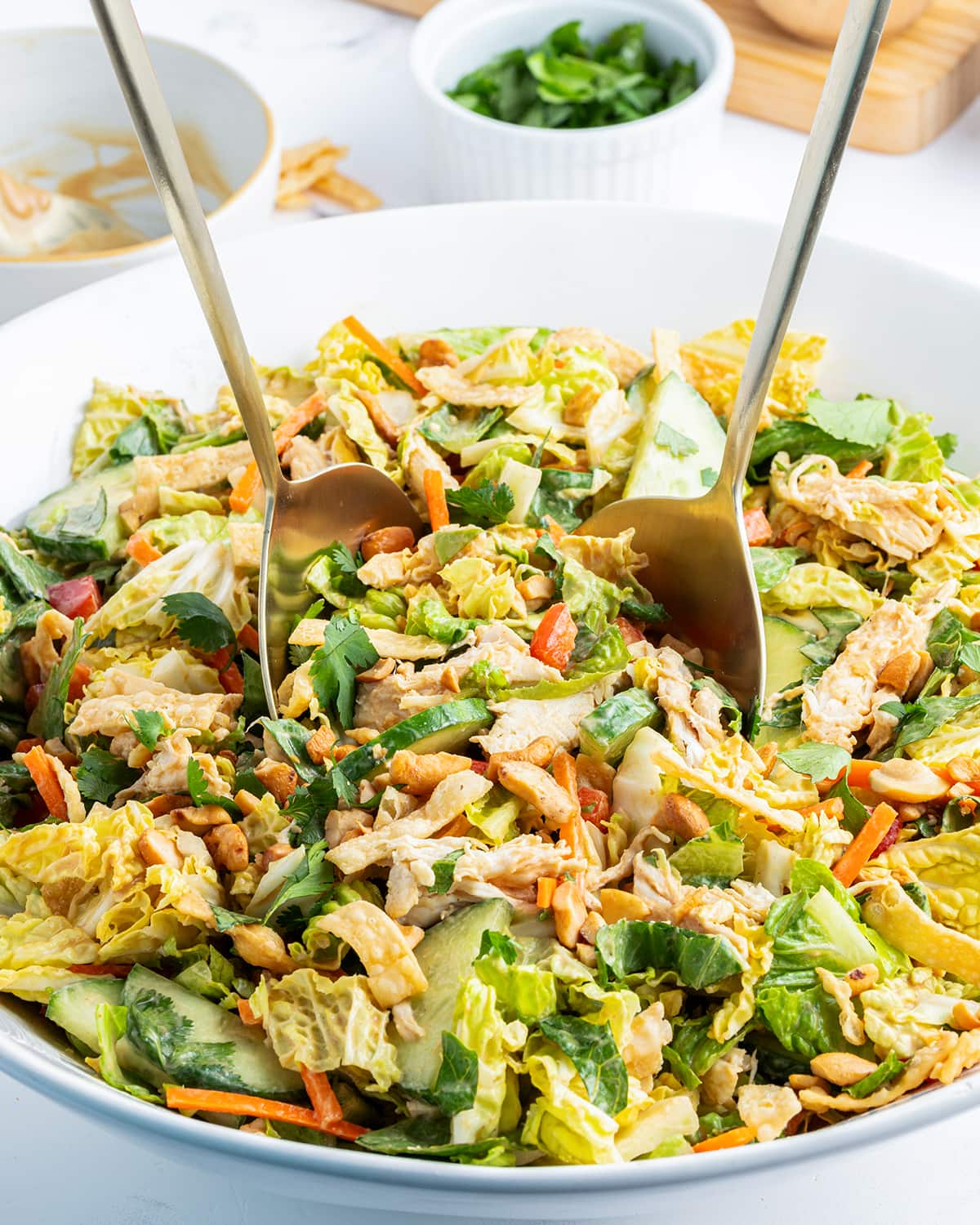 A bowl of Thai chicken salad with two mixing spoons in it.