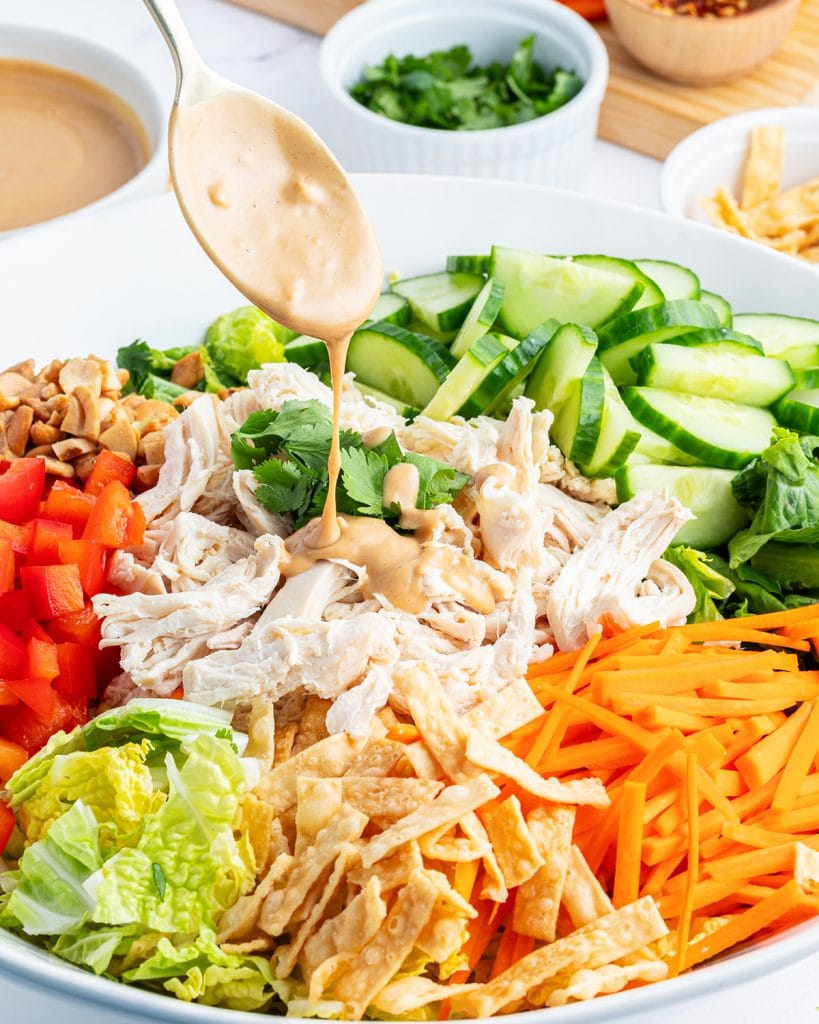 Sweet peanut salad dressing being drizzled from a spoon onto salad.
