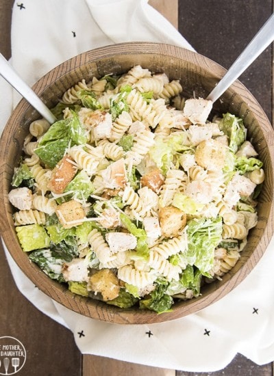 A wooden bowl full of chicken caesar pasta salad.