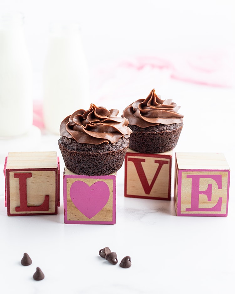 Blocks spelling out the word love in pink and red paint, the o is a heart. There is a chocolate cupcake on top of the heart block and the v block.