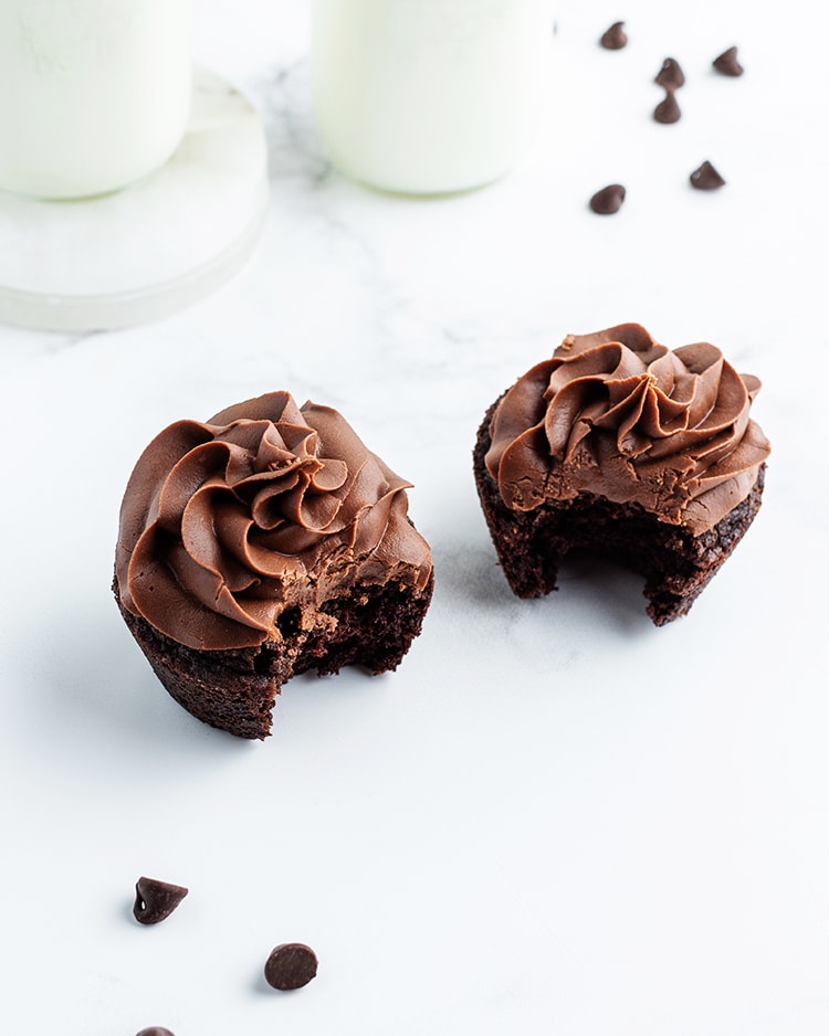Two chocolate cupcakes with chocolate frosting, and they both have a bite taken out of them.