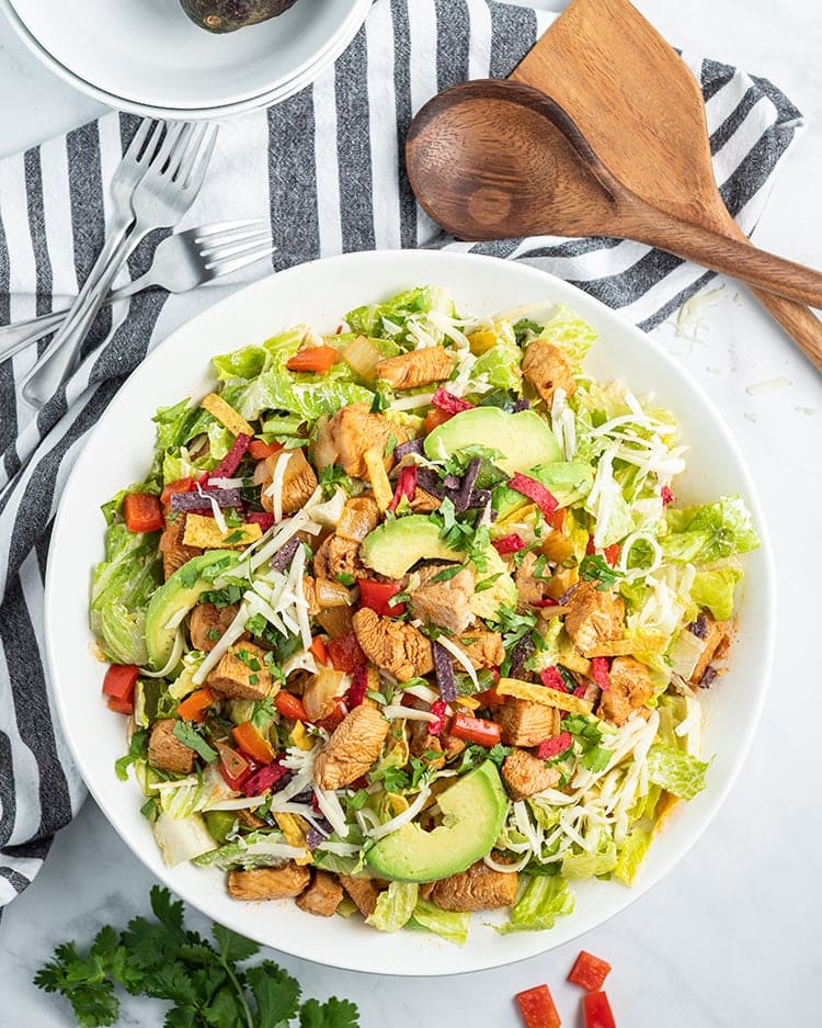 Above image of chicken fajita salad in a white bowl with wooden spoons and forks surrounding it.