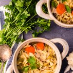 Above image of chicken noodle soup in white bowls with ingredients surrounding them.