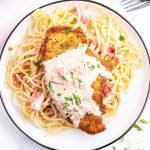 An overhead photo of an herb crusted chicken breast on spaghetti noodles, topped with a tomato cream sauce.