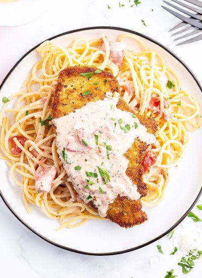 An overhead photo of an herb crusted chicken breast on spaghetti noodles, topped with a tomato cream sauce.