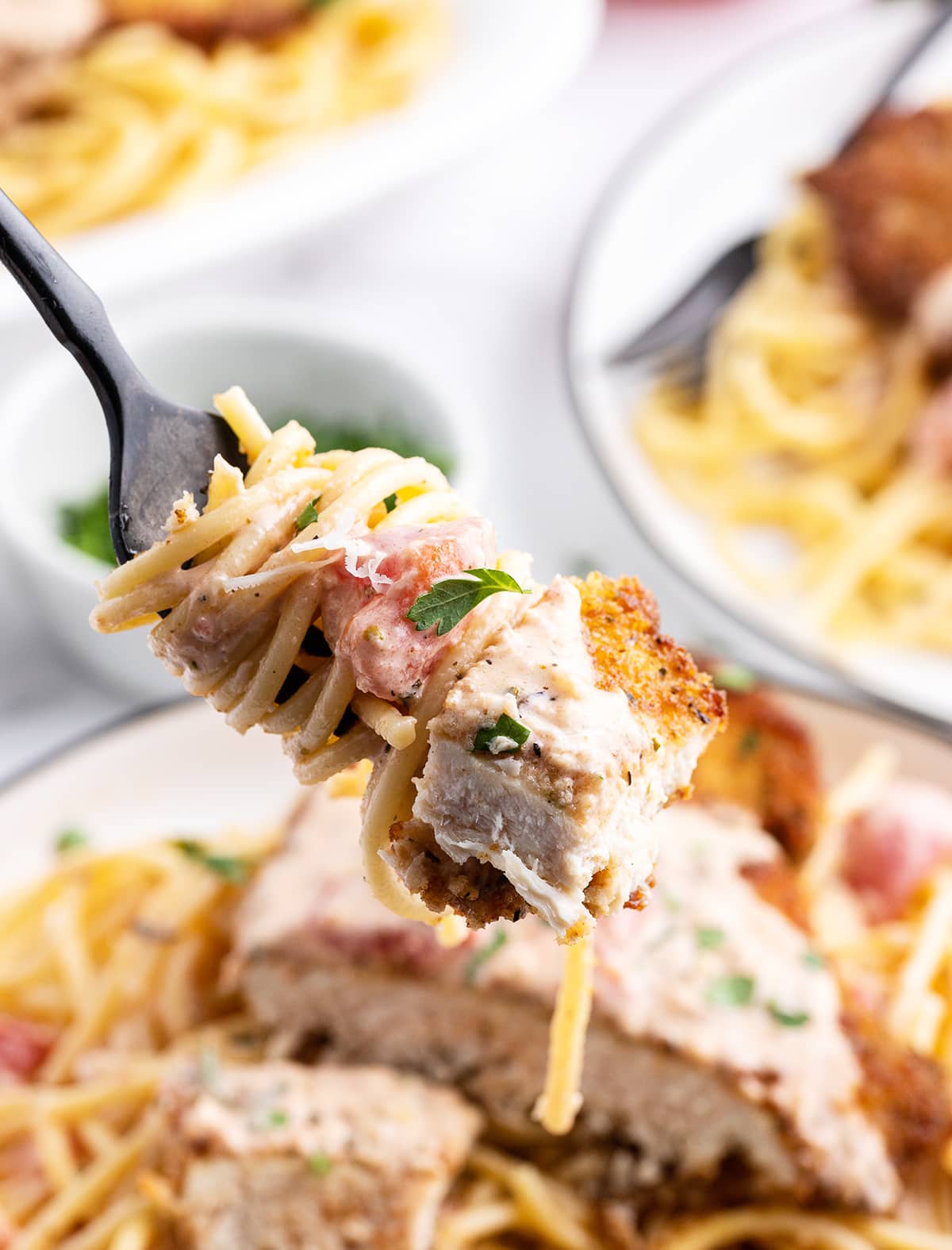 A bite of chicken and spaghetti noodles wrapped on a fork, with a creamy tomato sauce, and fresh parsley on top.