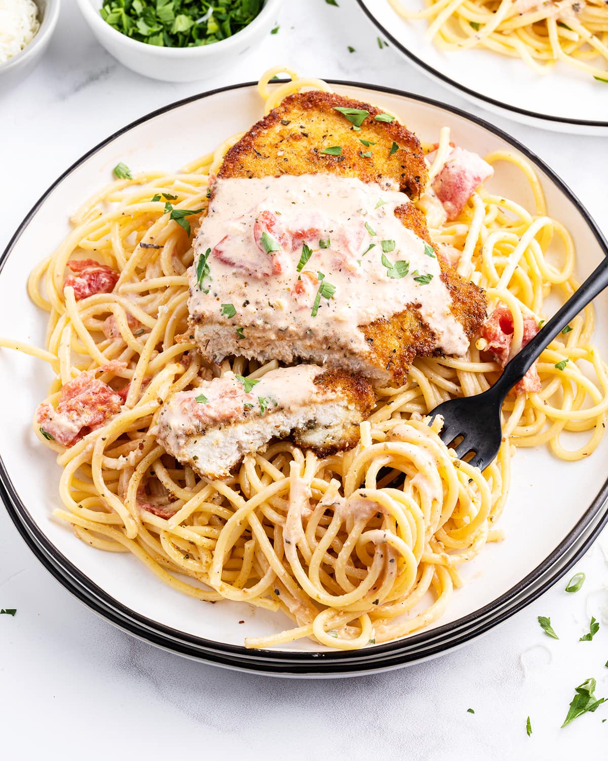 A plate of spaghetti noodles topped with a breaded chicken breast, all topped with a tomato cream sauce. The chicken is cut with a piece in front of the breast.