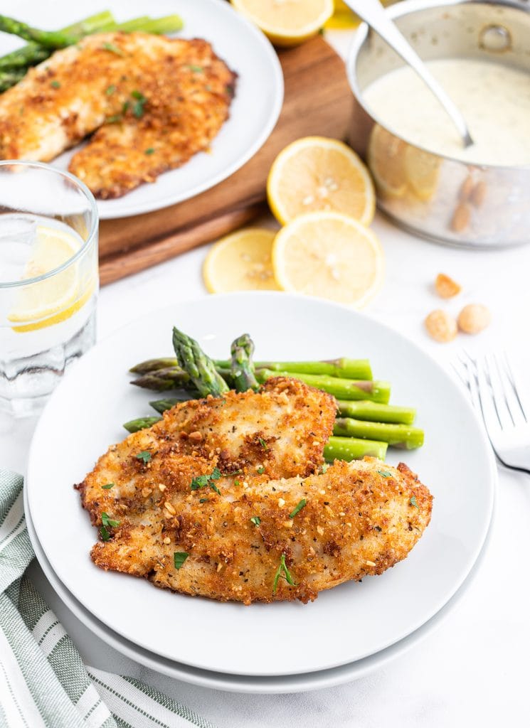 A macadamia crusted tilapia fillet on a plate next to asparagus.