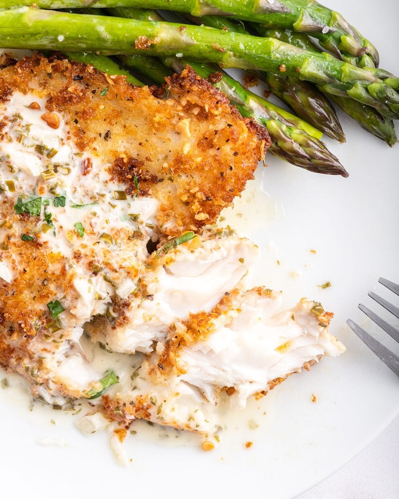 A macadamia nut crusted tilapia filet on a plate with a few pieces cut off