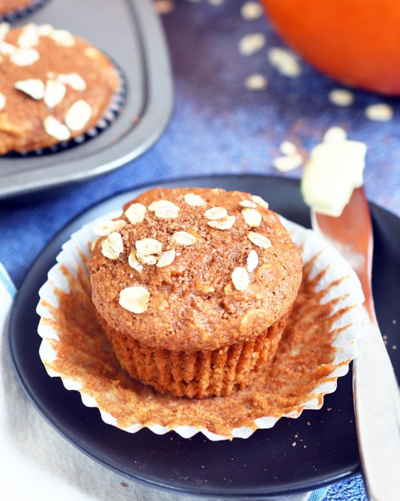 pumpkin oat muffin in a open muffin liner on a brown plate along side a butter knife with butter 