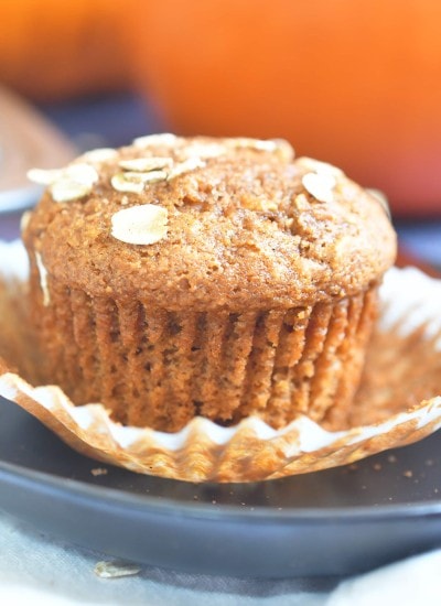 pumpkin oat muffin on a paper liner on top of a brown plate with an orange pumpkin in the background