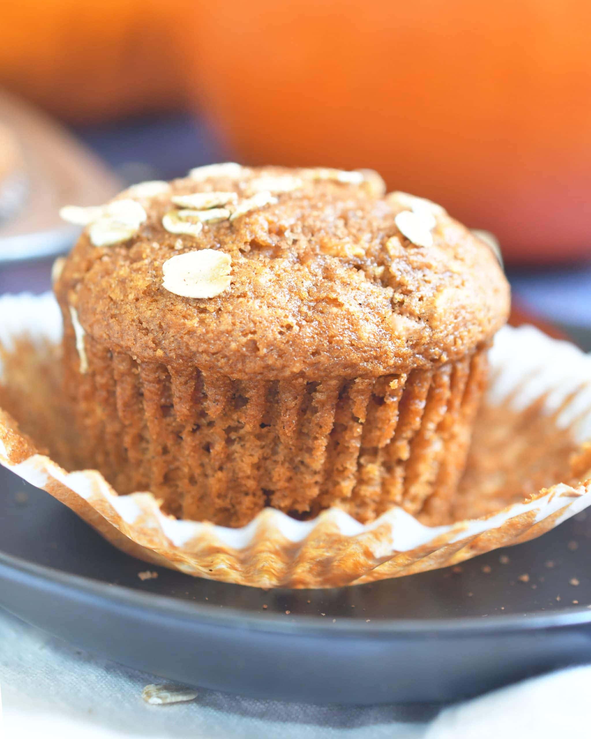 pumpkin oat muffin on a paper liner on top of a brown plate with an orange pumpkin in the background