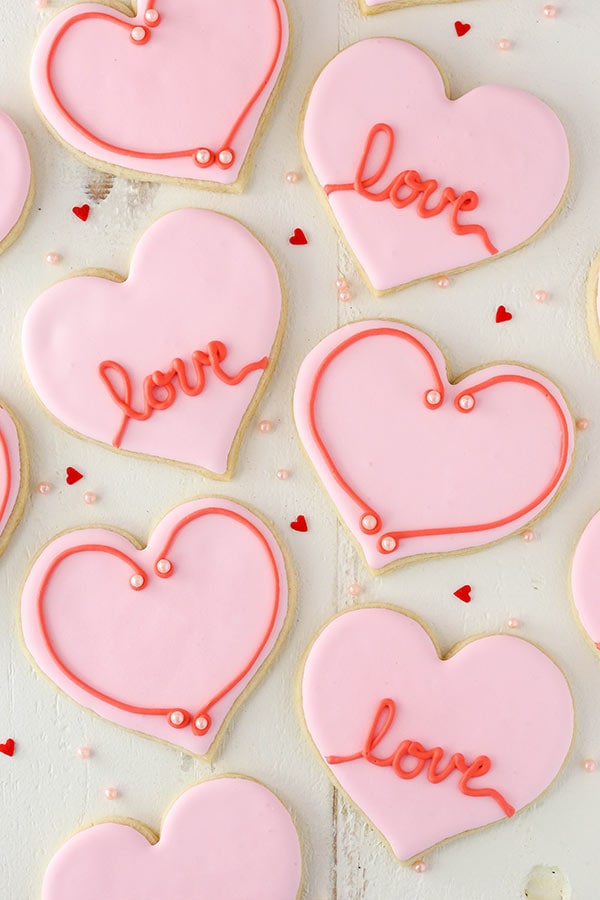 Above image of valentine\'s day cutout cookies with pink and red frosting with love written on them.